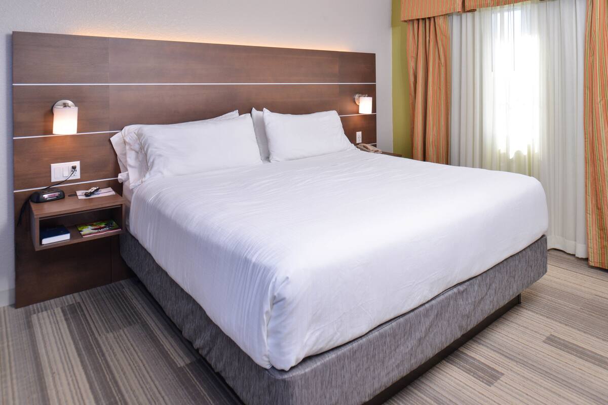 A large bed with white linens, a wooden headboard, bedside lamps, a nightstand with a book and a phone, and a striped carpet.