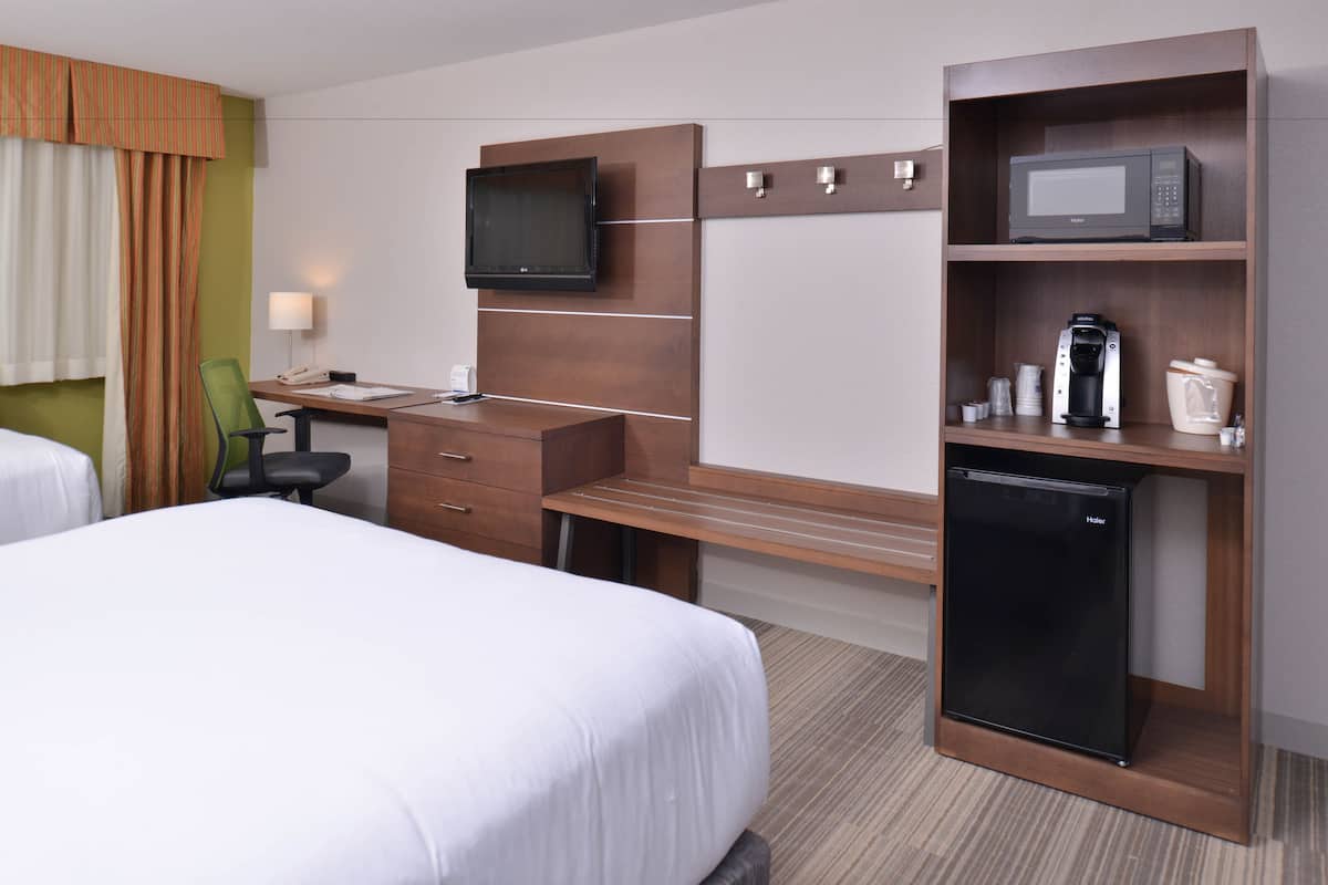 A hotel room with two beds, a desk with a chair, a television, a microwave, a coffee maker, and a mini-fridge.