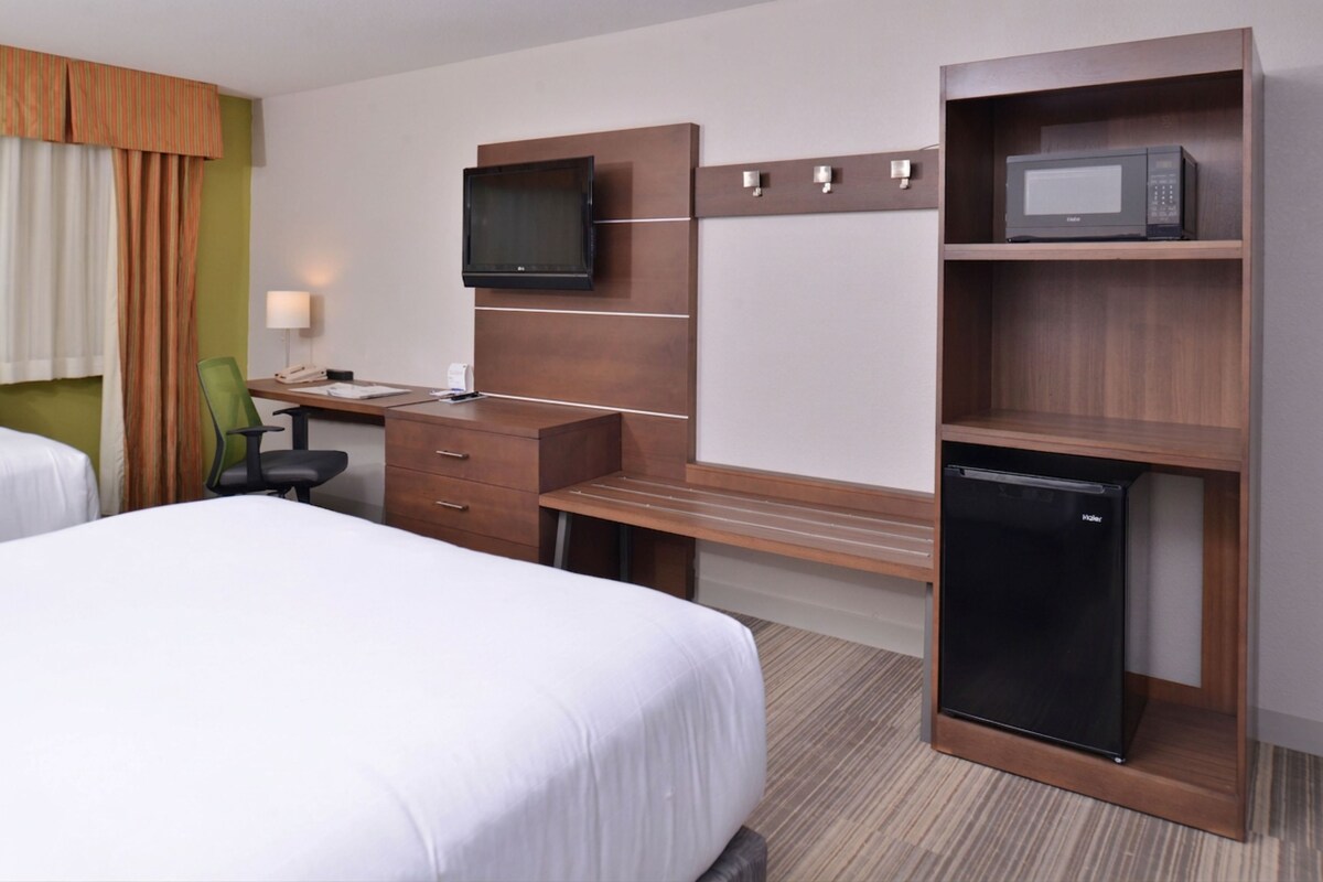 Une chambre d’hôtel avec deux lits, un bureau avec une chaise, une télévision, un four à micro-ondes et un réfrigérateur.