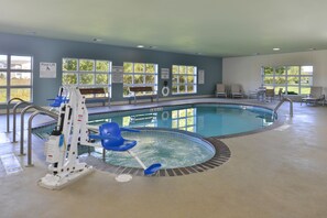 An indoor swimming pool with a pool lift, lounge chairs, and a bench. - Holiday Inn Express and Suites Stevens Point by IHG (Stevens Point)