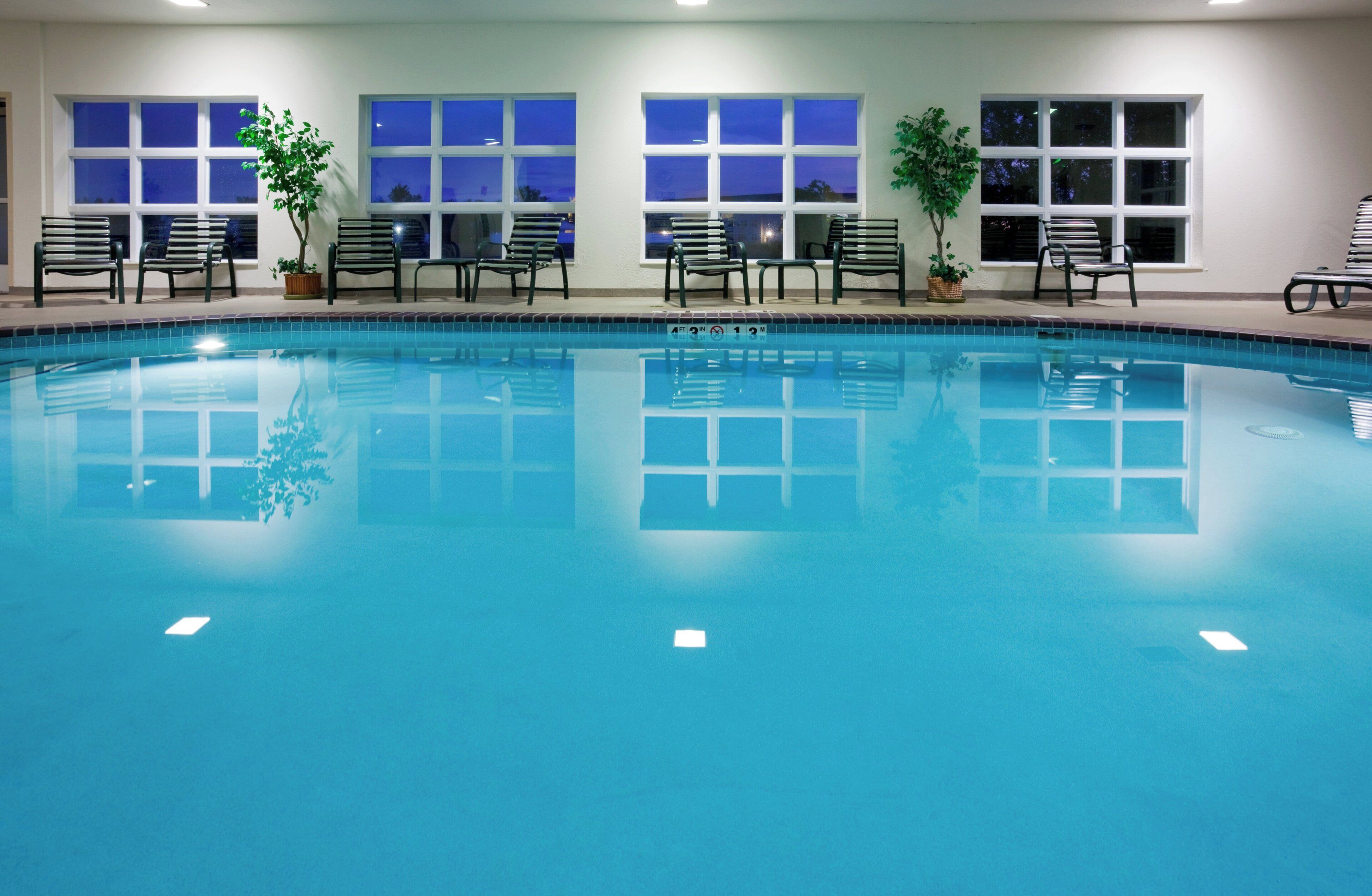 An indoor swimming pool with multiple benches and potted plants around the perimeter.