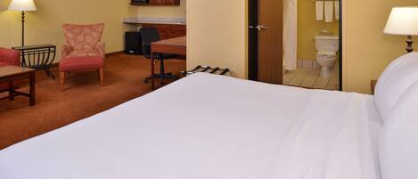 A hotel room with a large bed, a desk, a chair, and a kitchenette.