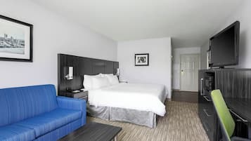 Ett hotellrum med en säng, en blå soffa, ett skrivbord, en tv och en tavla på väggen.
