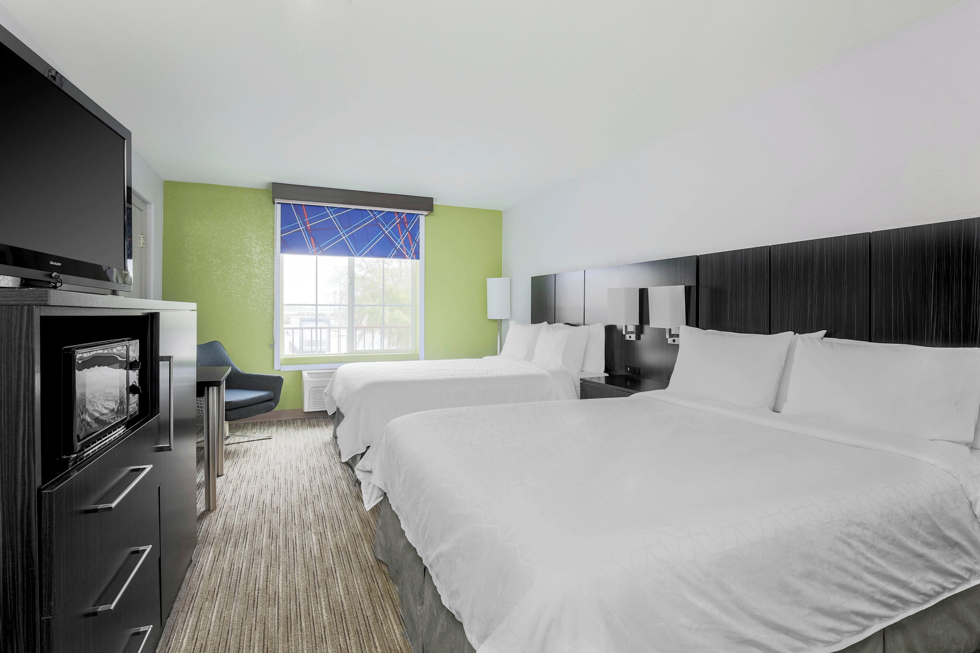 A hotel room with a large bed, a TV, a desk, and a chair.