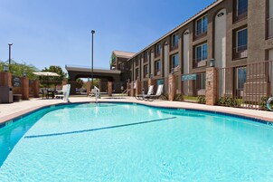 Una piscina con sillones de descanso y un edificio con varias ventanas y balcones.