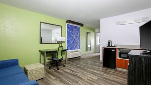 Camera d'albergo con parete verde, divano blu, scrivania con sedia, angolo cottura e televisore.