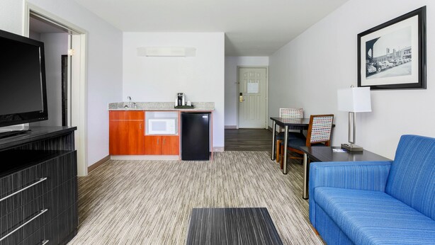 A compact hotel room with a kitchenette, a flat-screen TV, a blue sofa, and a framed picture on the wall. - Holiday Inn Express Lancaster by IHG (Lancaster)