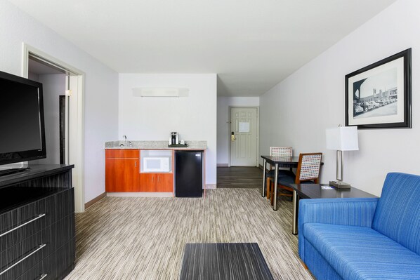 A compact hotel room with a kitchenette, a flat-screen TV, a blue sofa, and a framed picture on the wall. - Holiday Inn Express Lancaster by IHG (Lancaster)
