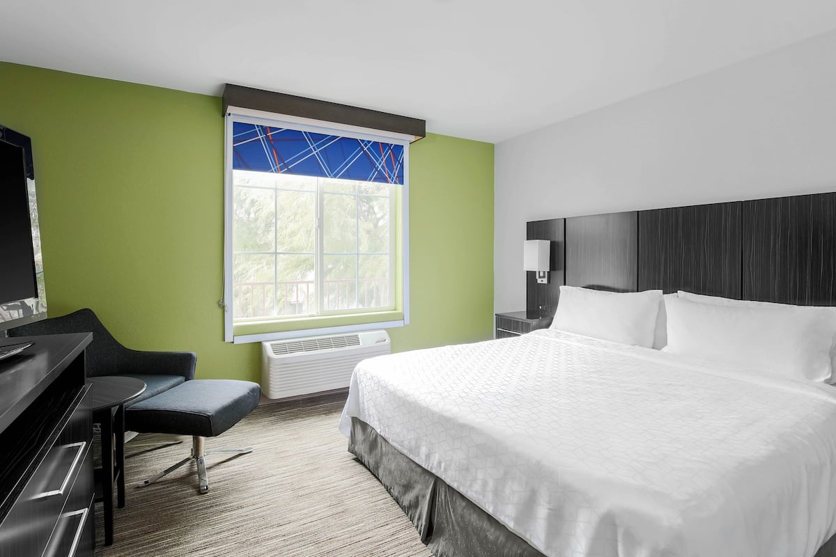 Habitación de hotel con una cama grande, un escritorio, una silla y una ventana con persianas.