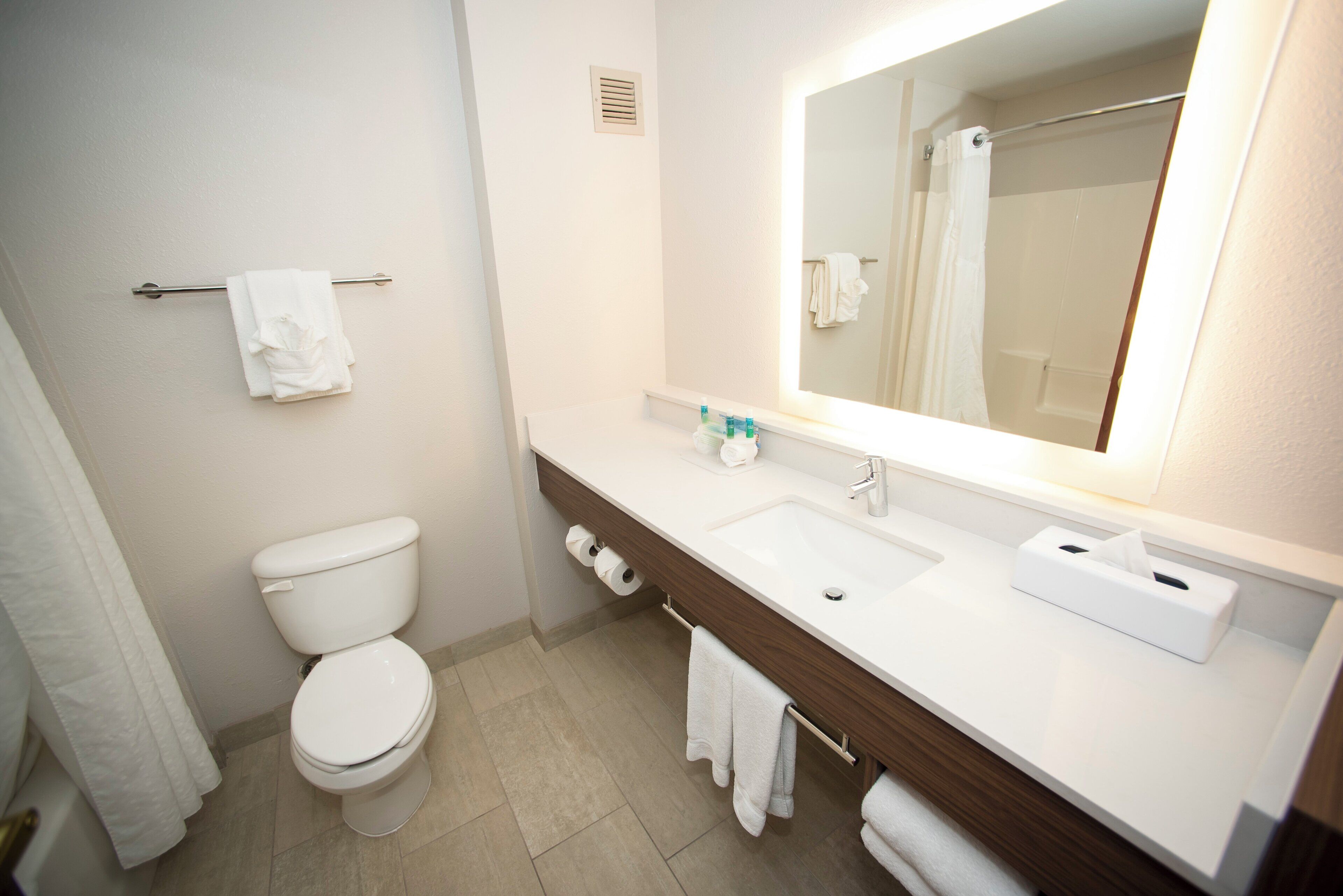A bathroom with a toilet, sink, mirror, towel rack, and a shower curtain.