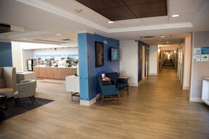 Un hall de hotel con mostrador de recepción, zona de estar y un pasillo que conduce a otras habitaciones.