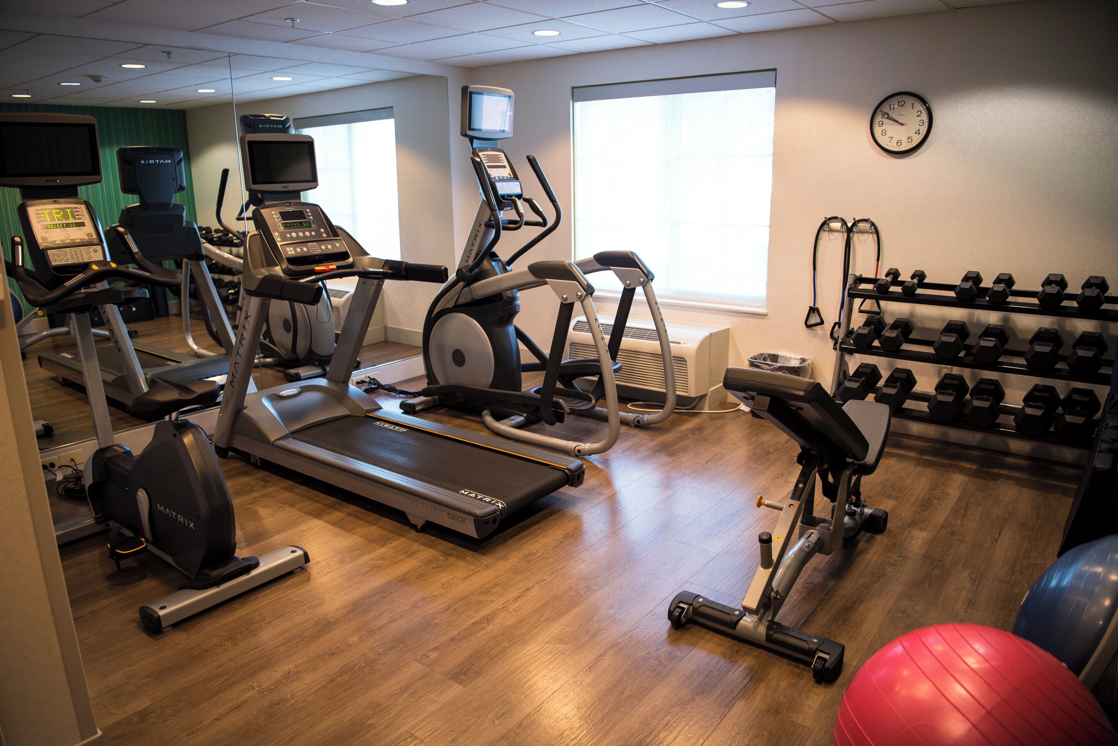 A gym with treadmills, elliptical machines, a weight bench, and a rack of dumbbells.