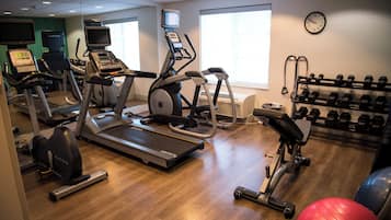 A gym with treadmills, elliptical machines, a weight bench, and a rack of dumbbells.