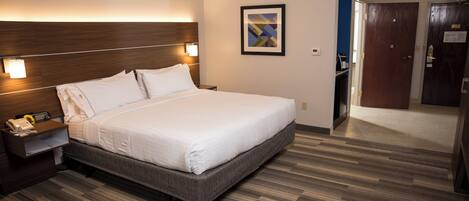 A hotel room with a large bed, bedside table with a lamp, a framed picture on the wall, and a wooden floor.