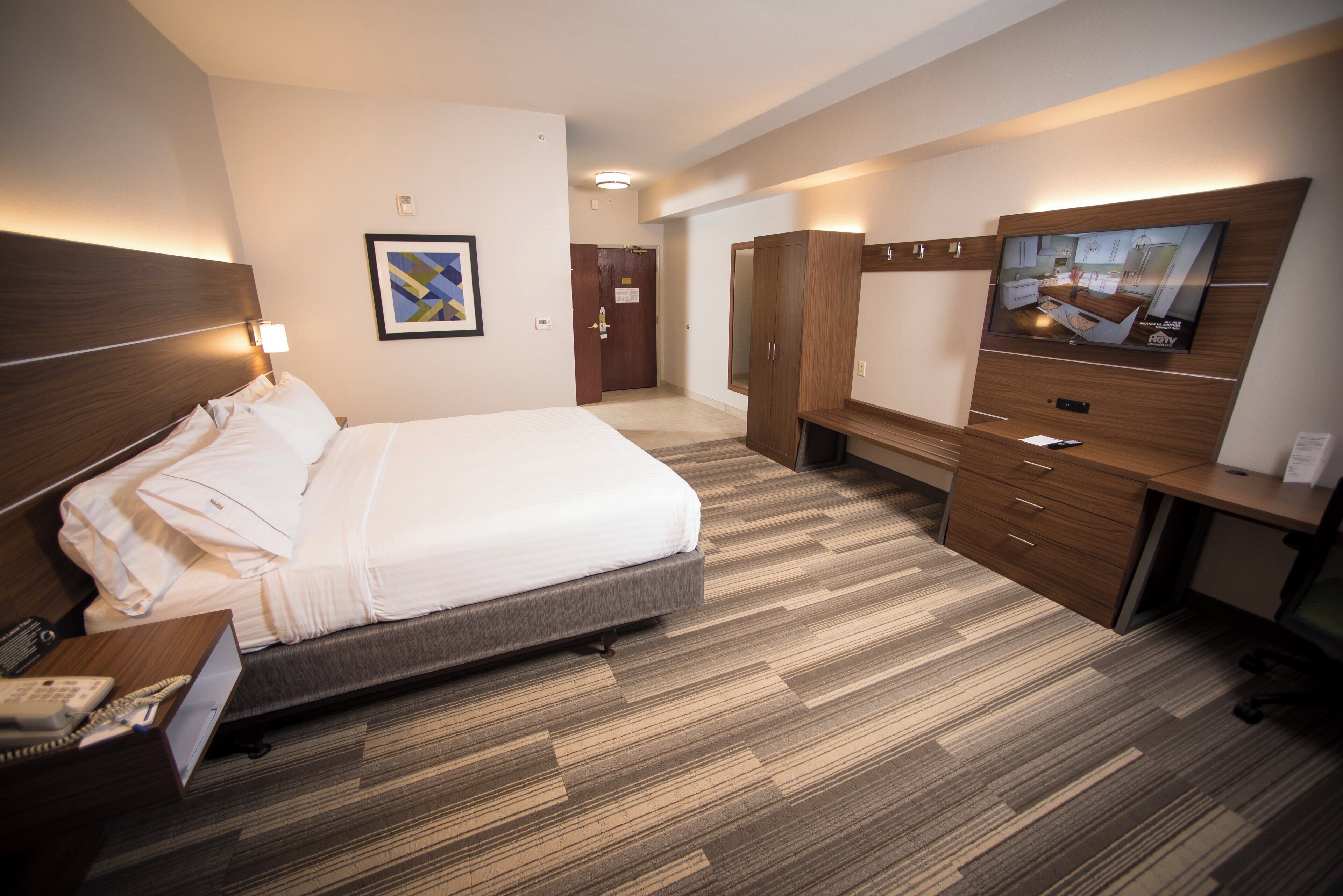 A hotel room with a bed, a desk, a TV, a wardrobe, and a framed picture on the wall.