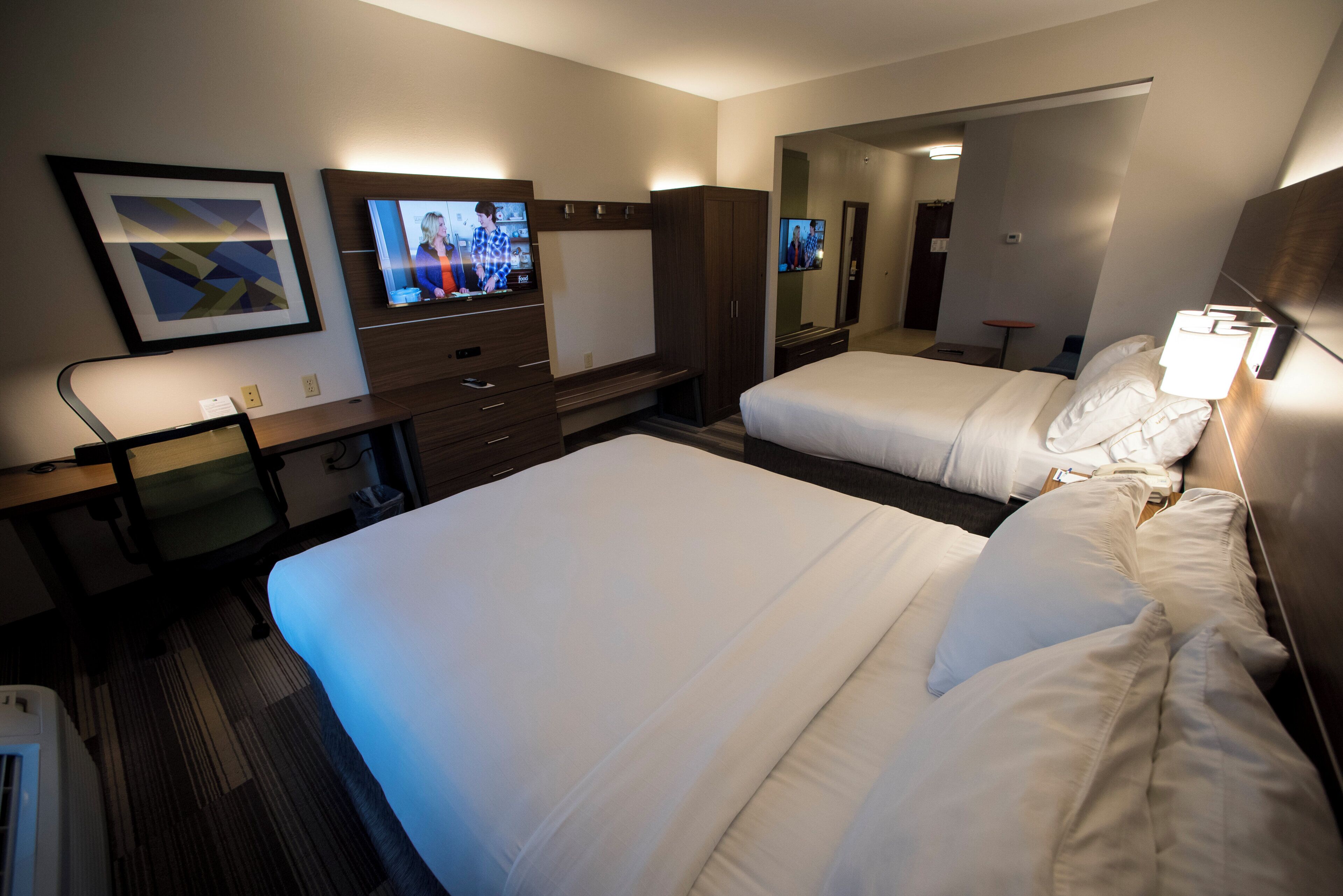 A hotel room with two beds, a desk with a computer, a TV, and a mirror.