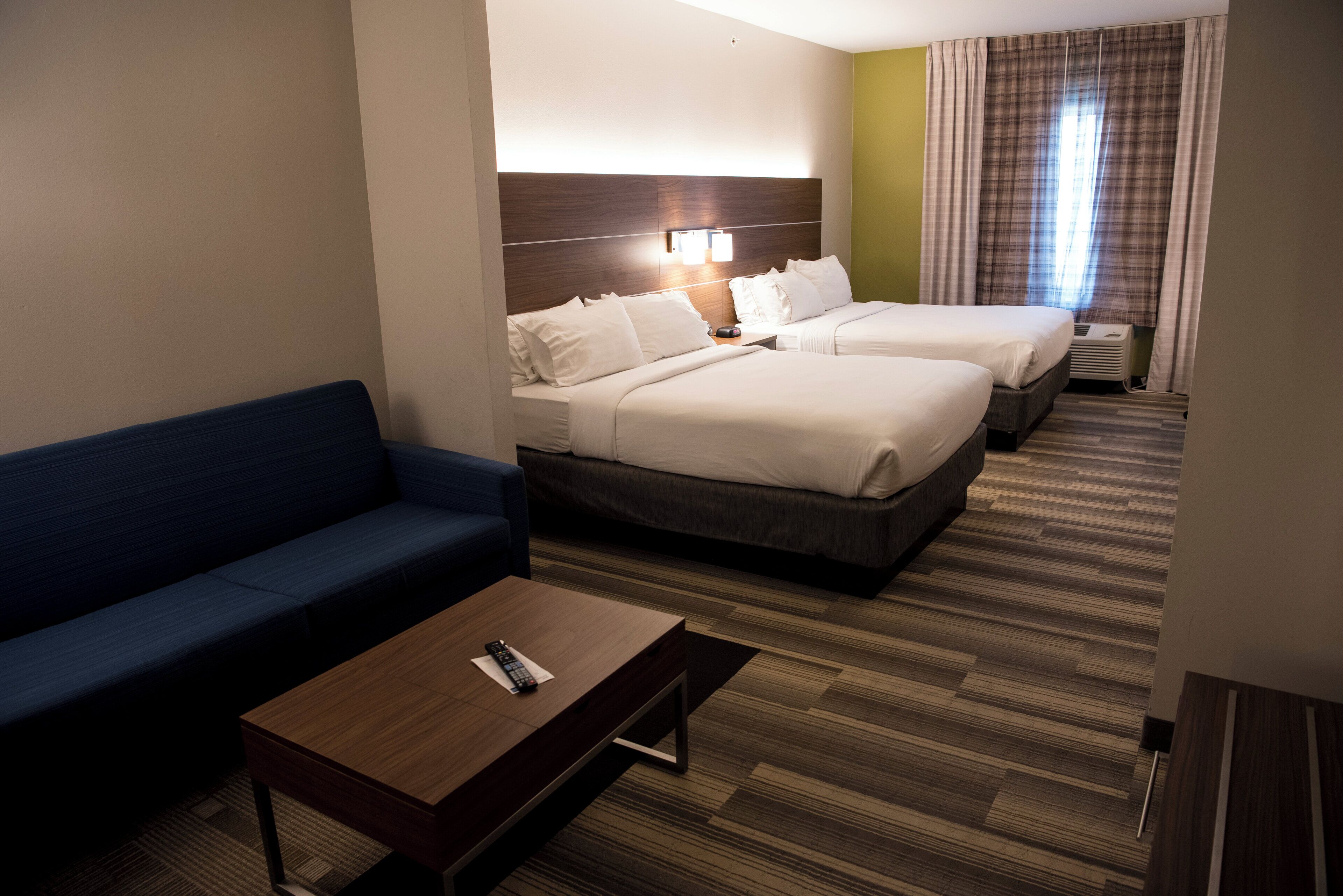 A hotel room with two beds, a sofa, a coffee table, and a window with curtains.