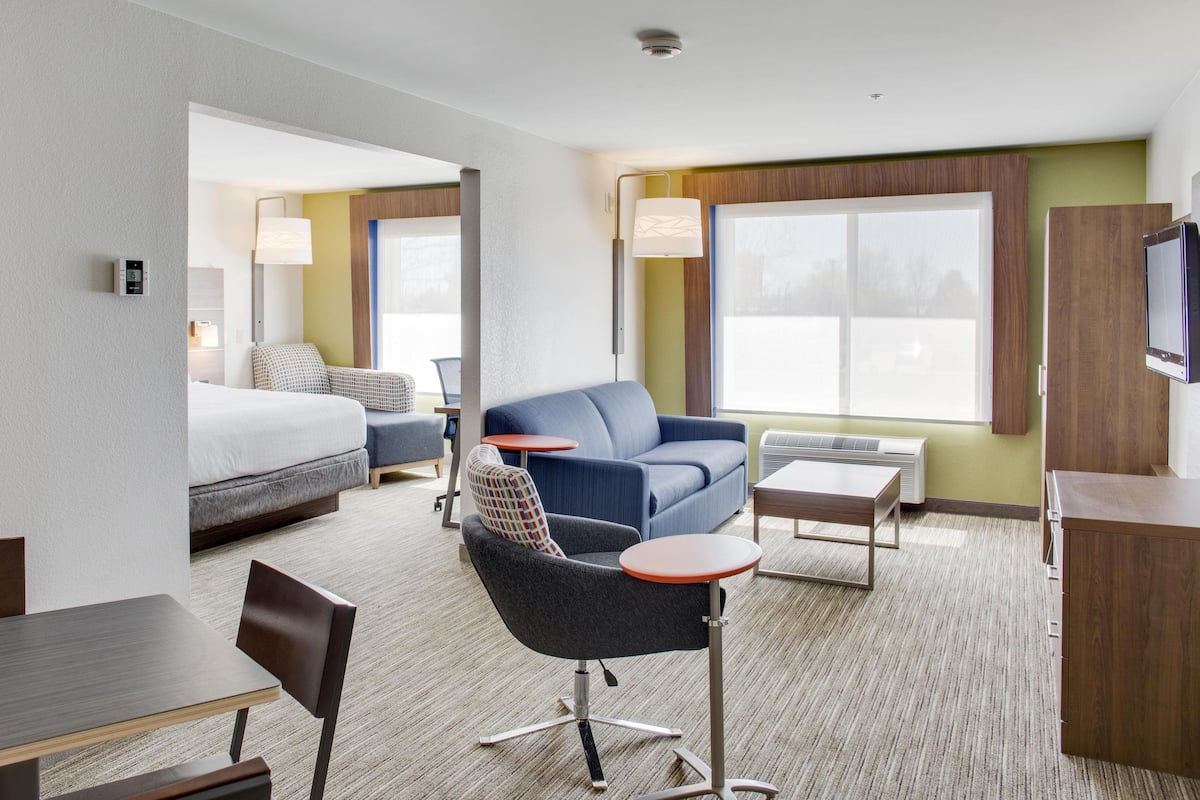 A hotel room with a bed, a blue sofa, a small table, a chair, and a TV.