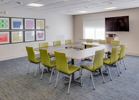 Un salón de conferencias con una gran mesa, sillas, una televisión de pantalla plana y cuadros en la pared.
