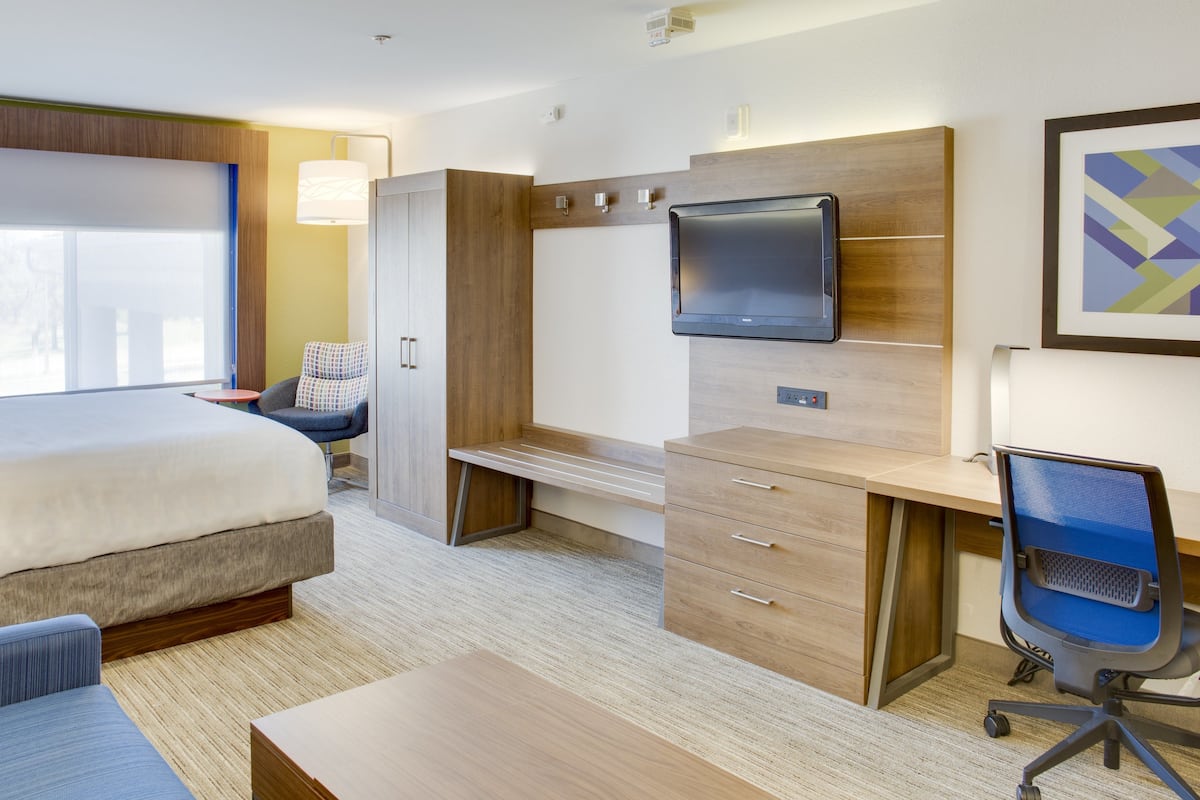 A modern hotel room with a bed, desk, chair, and TV.