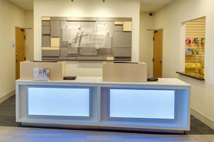 A hotel reception desk with a modern design, featuring a large illuminated sign above the desk and a small display case with brochures.