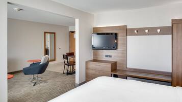 A hotel room with a bed, a desk with a flat-screen TV, a chair, and a small table.