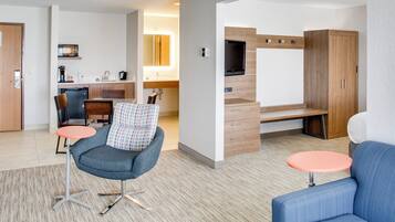 A modern hotel room with a kitchenette, a flat-screen TV, a sofa, and a small table.
