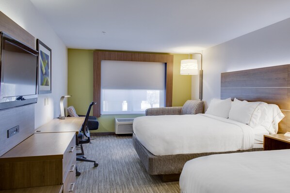 A hotel room with a bed, a desk with a chair, a TV, and a window with blinds.