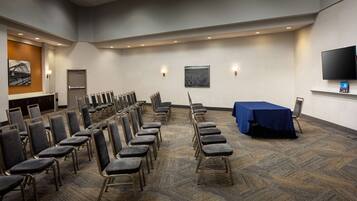 A conference room with rows of chairs, a table with a blue tablecloth, and a flat-screen TV mounted on the wall.