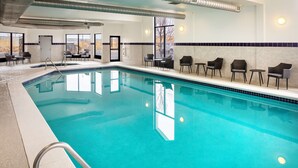 An indoor swimming pool with clear blue water, surrounded by lounge chairs and tables, with a view of the outdoors through large windows. - Hampton Inn & Suites Parker (Parker)