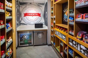 Zona de aperitivos y artículos varios, con microondas, refrigerador y estantes llenos de diferentes bocadillos y bebidas.