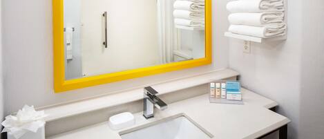 A bathroom with a white sink, a mirror with a yellow frame, and a shelf with folded towels.
