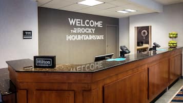 Una mesa de recepción con un cartel que dice "Bienvenido al Estado de las Montañas Rocosas", un cartel que indica "Gerente de Guardia" y un cartel de "Hilton Honors".