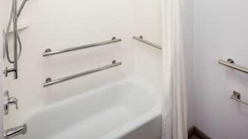 A bathroom with a white bathtub, a showerhead, and grab bars.
