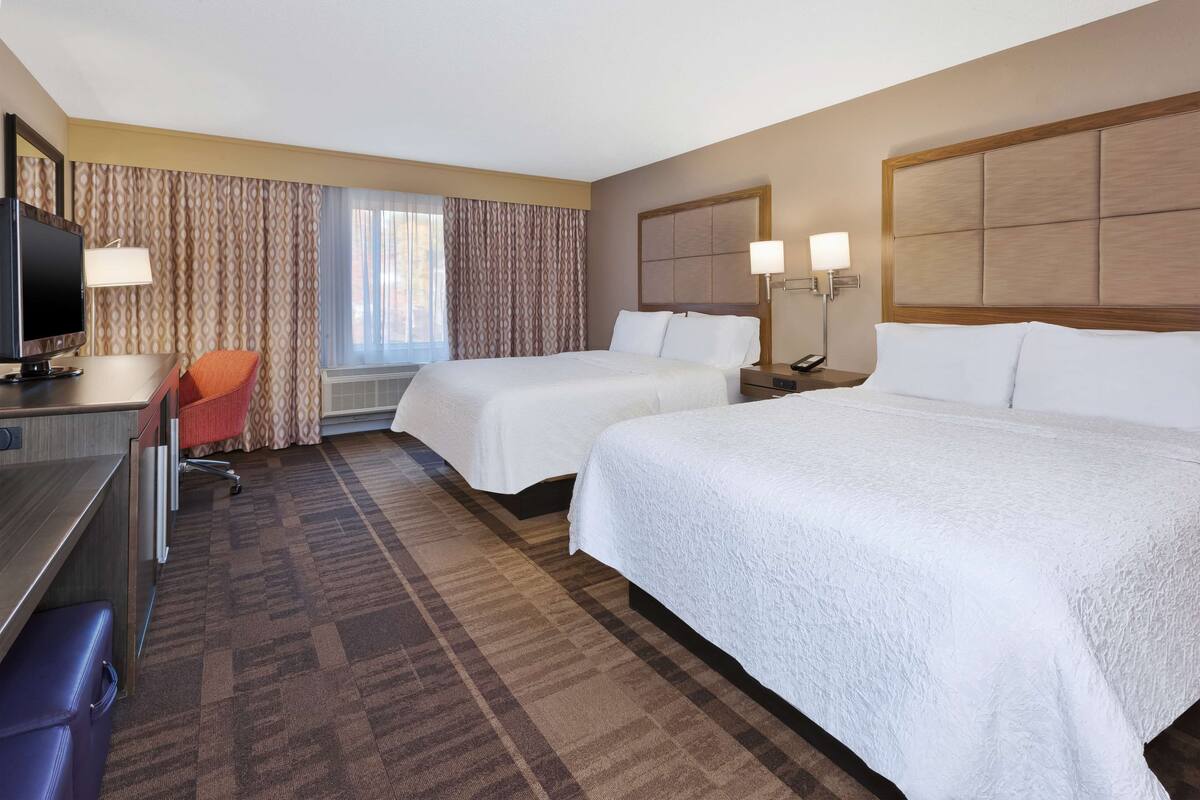 A hotel room with two beds, a desk with a computer, a chair, and a TV.