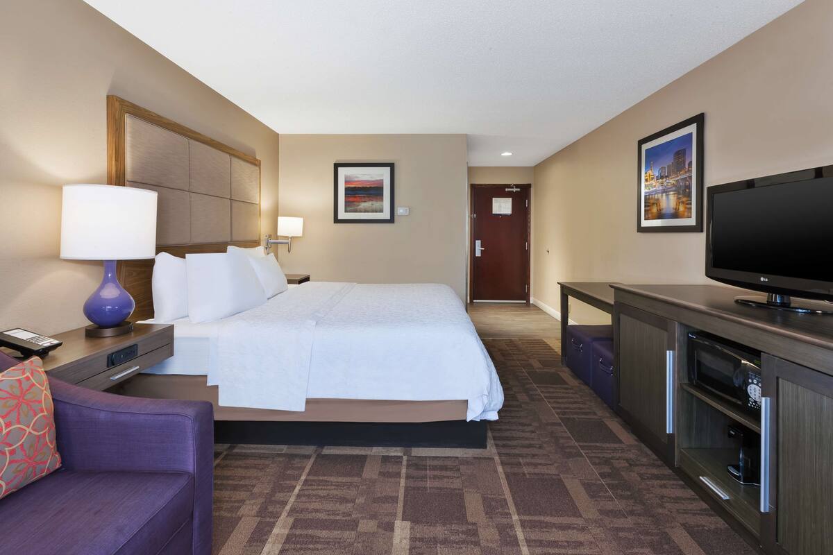 A hotel room with a bed, a TV, a desk, and a chair.