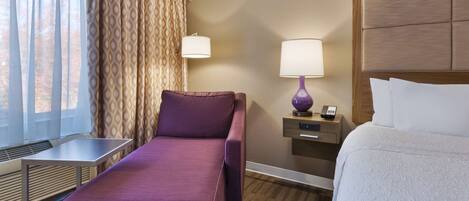 Habitación de hotel con cama, sofá, escritorio, lámpara y ventana con cortinas.