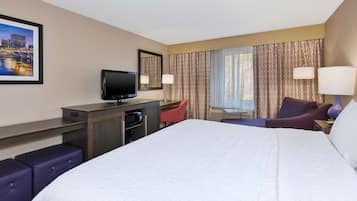 Een hotelkamer met een groot bed, een bureau met een flatscreen televisie, een stoel, een bank en een raam met gordijnen.