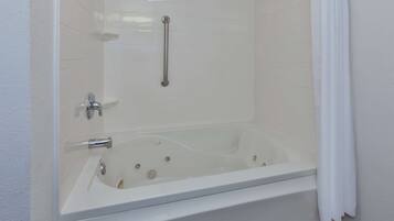 Une baignoire blanche équipée d’une pomme de douche, d’une barre d’appui et d’un rideau.