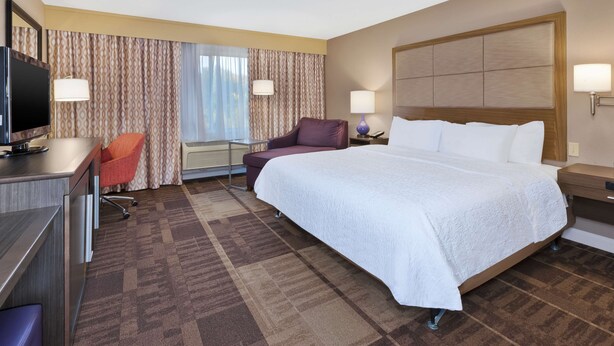 A hotel room with a large bed, a desk with a TV, a chair, and a window with curtains.