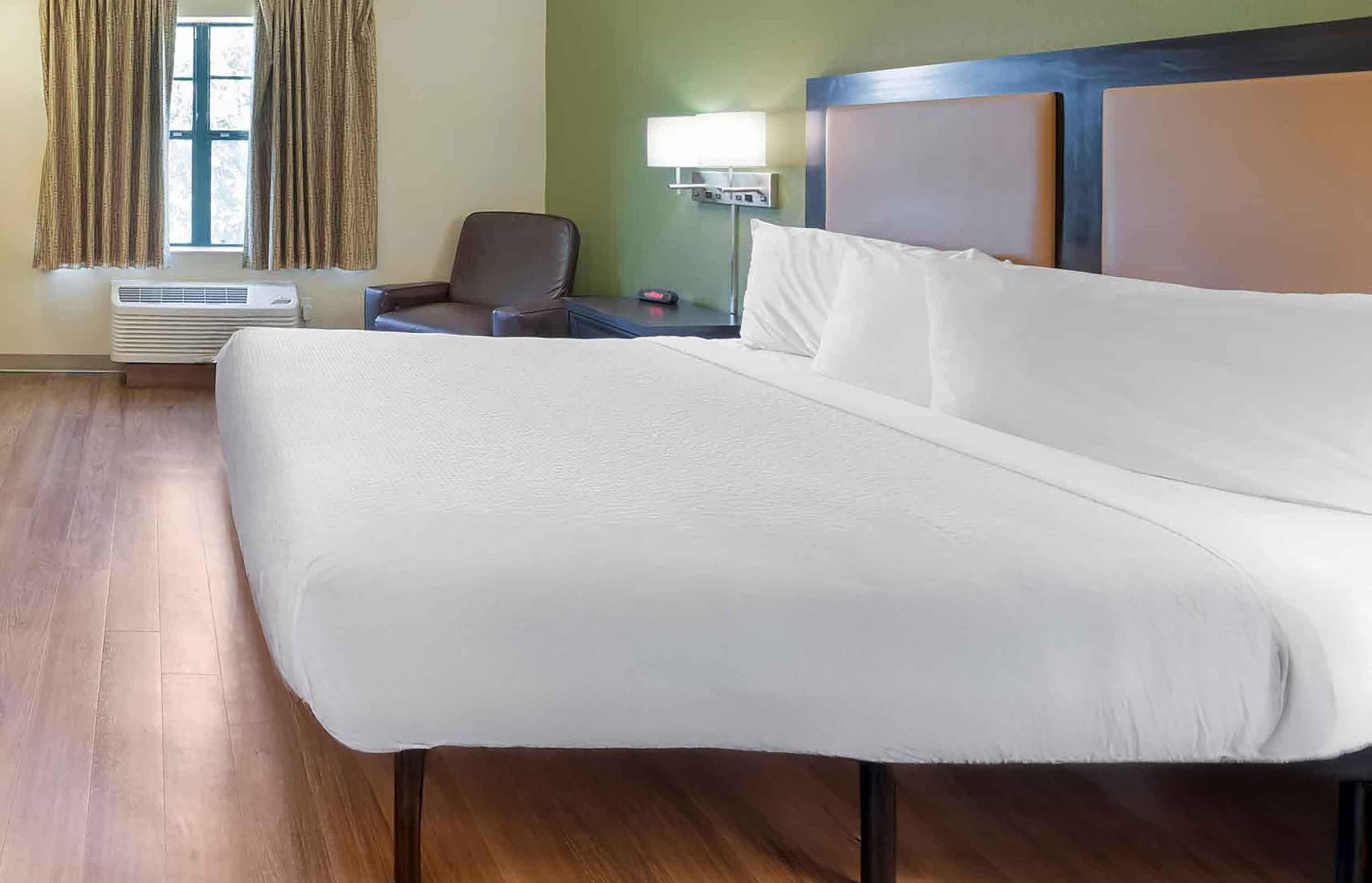 Habitación de hotel con una cama grande, una silla, una mesita de noche con lámpara y una ventana con cortinas.