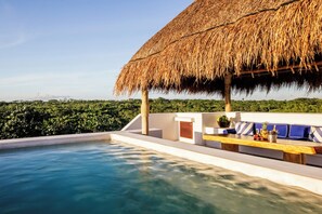 A poolside area with a thatched roof, a seating area with cushions, and a view of the greenery. - Hotel Esencia (Xpu-Ha)