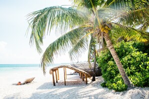 Une plage avec une structure recouverte de chaume, des palmiers et une vue dégagée sur l’océan.