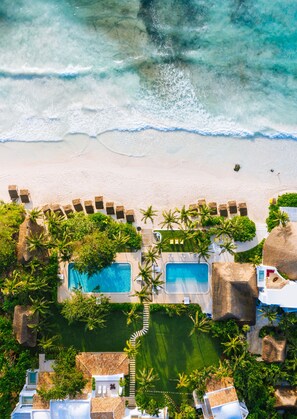 An aerial view of a resort with two swimming pools, a beach, and lush greenery. - Hotel Esencia (Xpu-Ha)