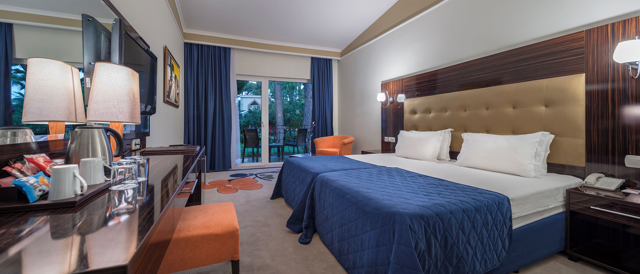 Habitación de hotel con cama, mesita de noche, lámpara y vistas al exterior.