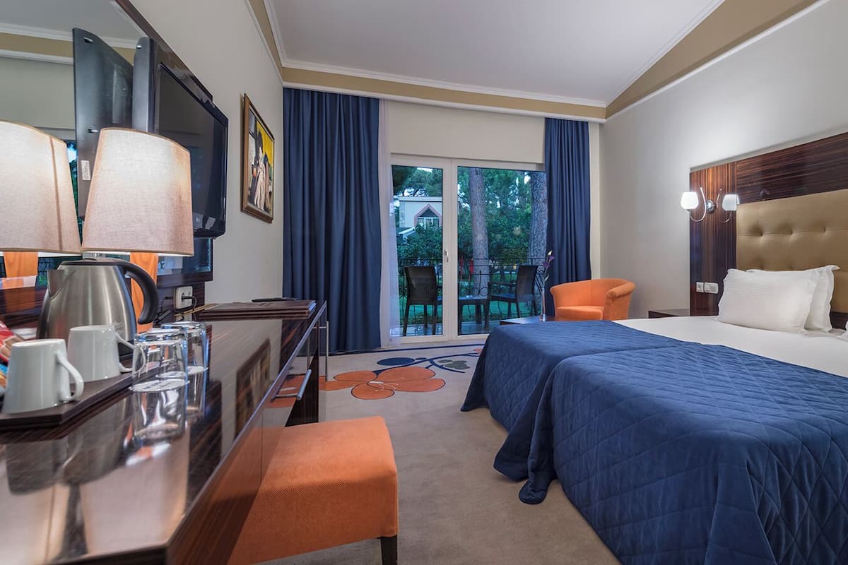 Habitación de hotel con cama, mesita de noche, lámpara y vistas al exterior.