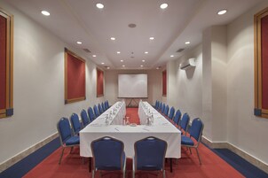 A conference room with a long table, blue chairs, and a projector screen.