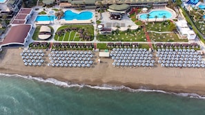 Oversigtsbillede af et resort med flere swimmingpools, en strand med mange parasoller og forskellige resortbygninger.
