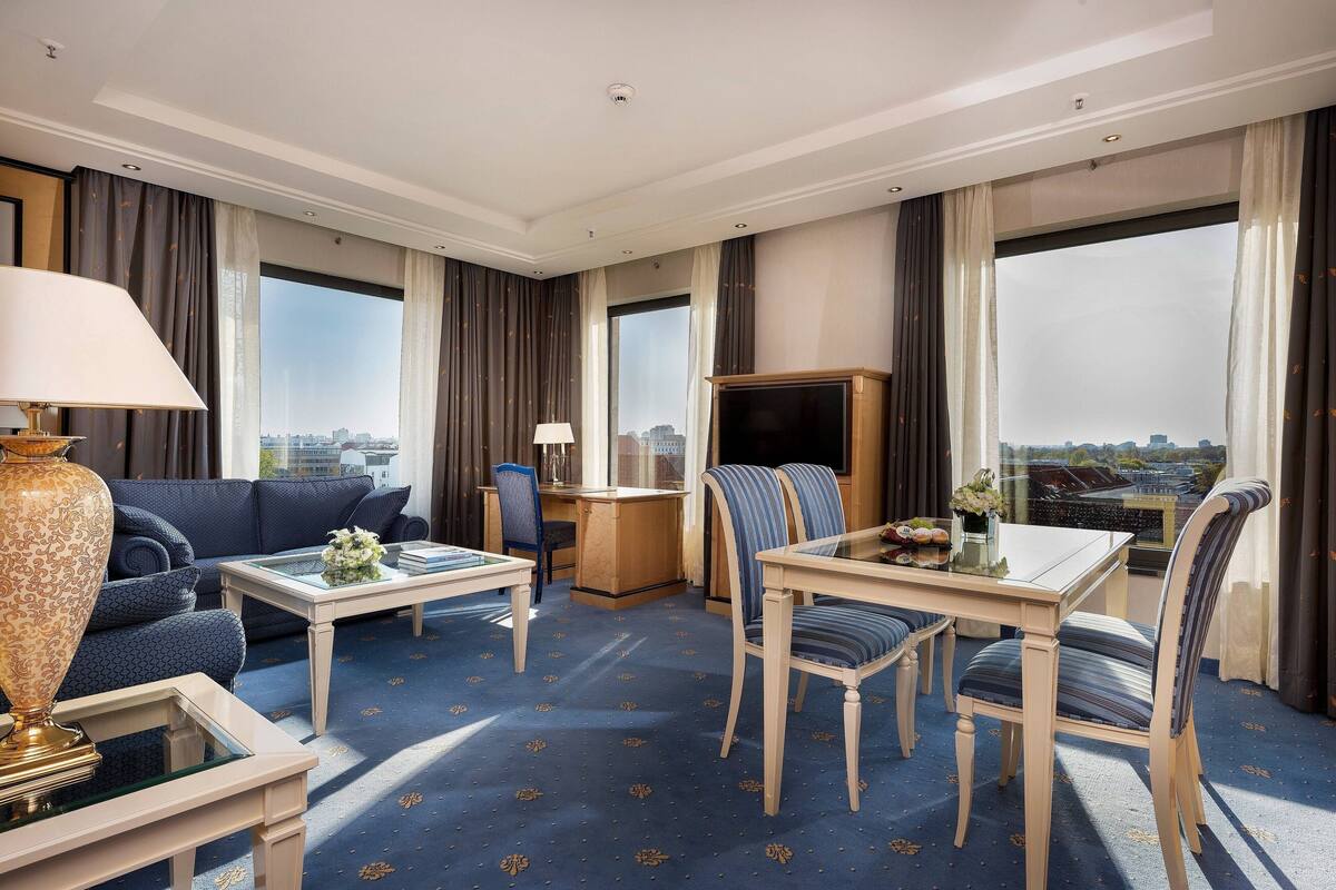 Ein Hotelzimmer mit großem Fenster, einer Couch, einem Esstisch und einem Fernseher.