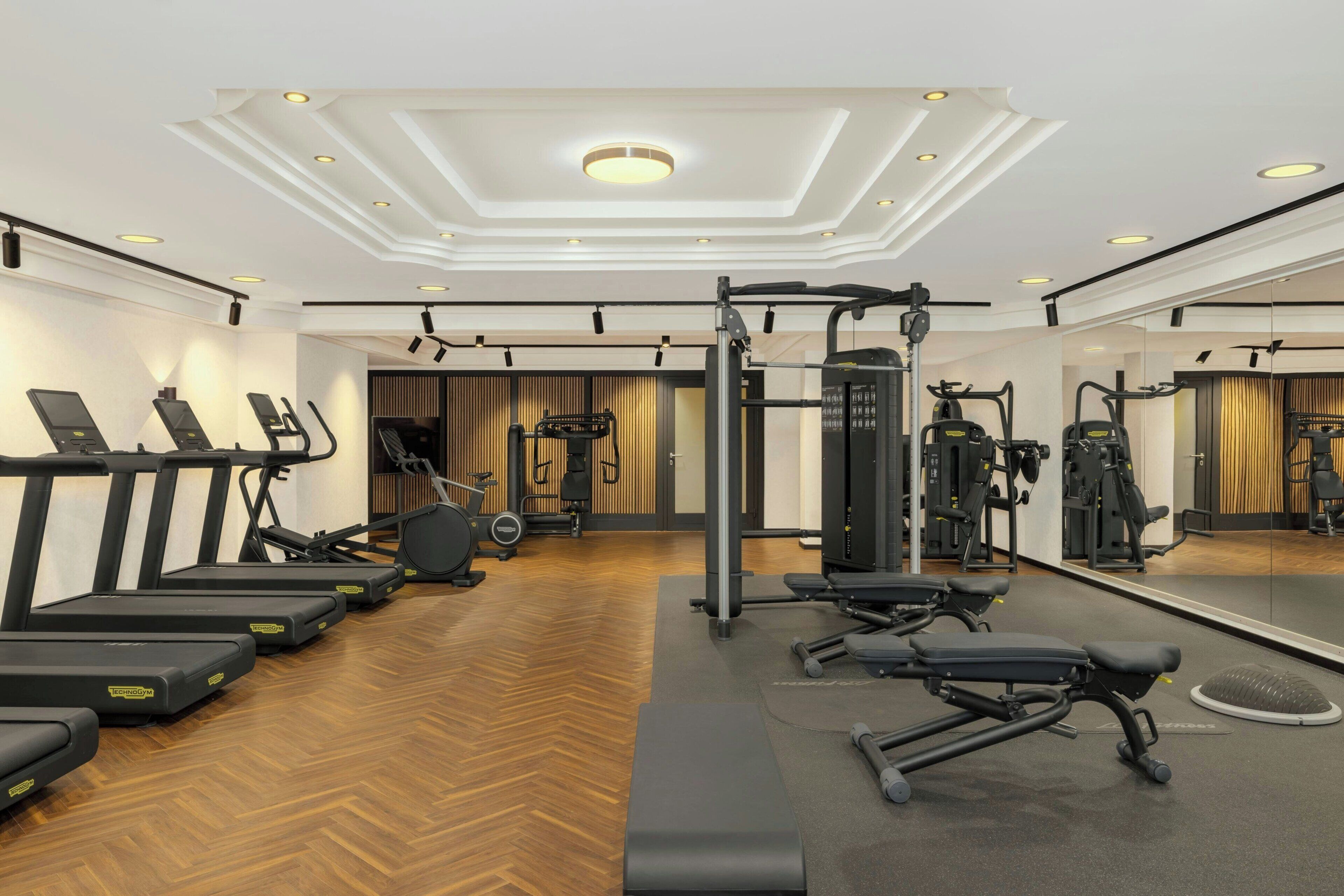 Un gimnasio moderno con cintas de correr, máquinas de pesas y un espejo grande.